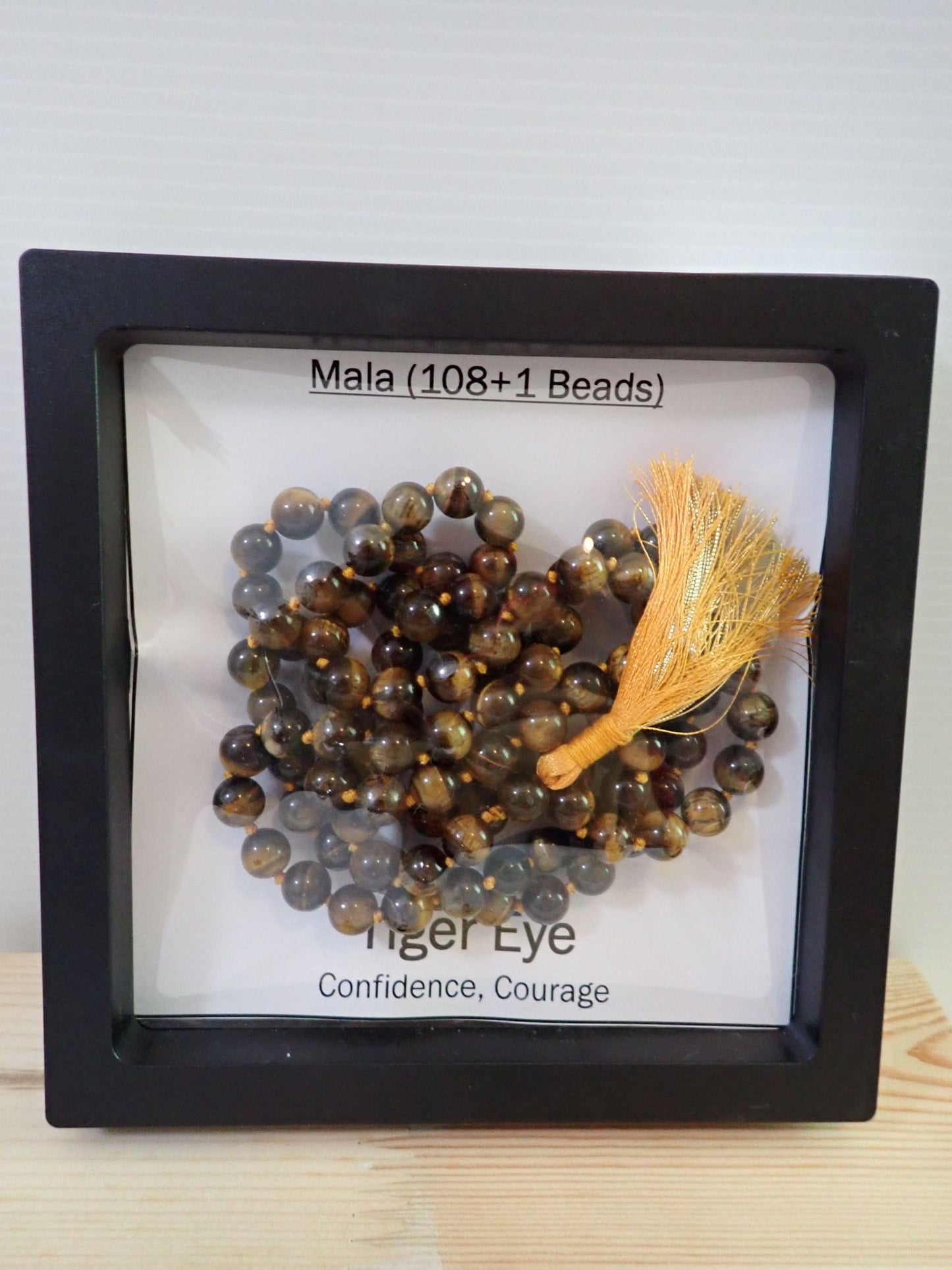 Tiger Eye Mala with golden tassel on wooden stand