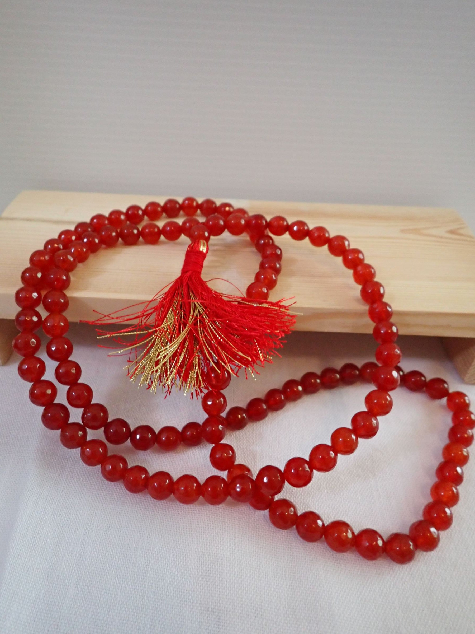 Red Agate Mala 108+1 beads with red and gold tassel on wooden stand