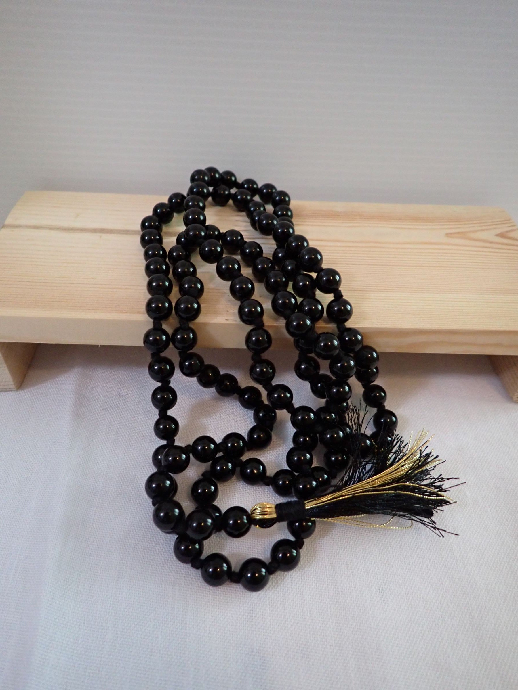 Black Agate Mala 108+1 beads with black and gold tassel on wooden stand