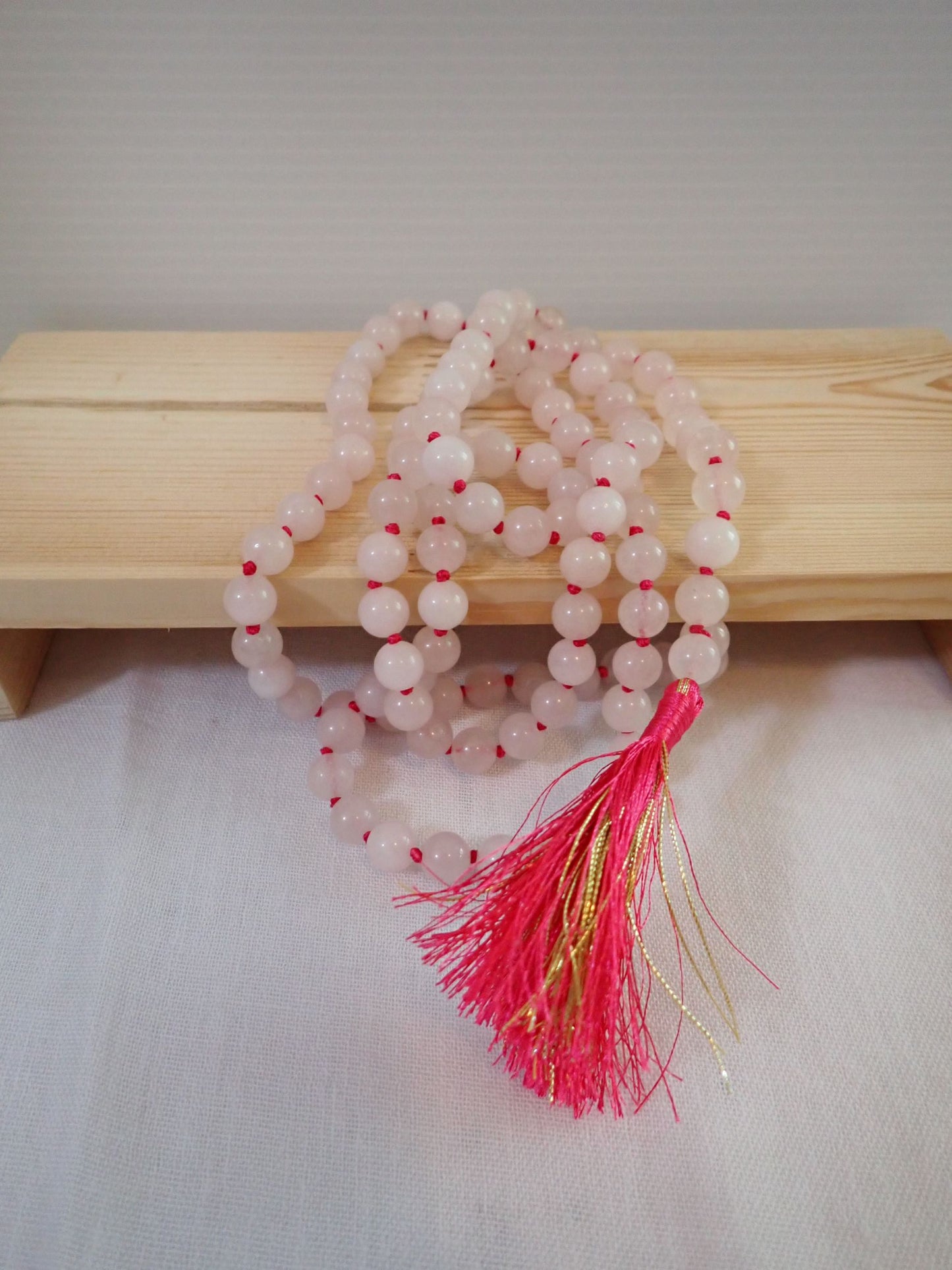 Rose Quartz Mala 108+1 beads with pink and gold tassel on wooden stand